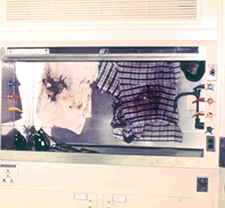 various articles of clothing with stains and residues, hanging in enclosed structure.