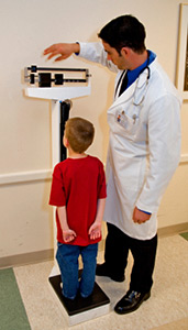 Boy in a doctor's office, standing on a scale as the doctor moves the sliders to determine the boy's weight.