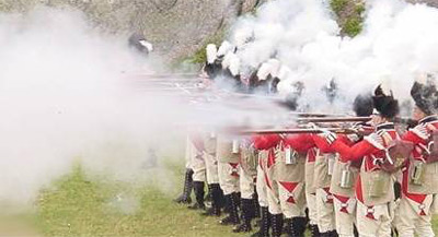 Historical reinactment of British redcoat soldiers firing black powder rifles.