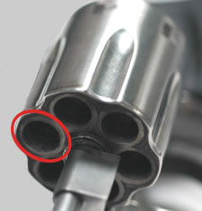 Close-up view of open cylinder on revolver handgun with halo on individual chamber highlighted.