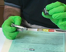 Laboratory technician wearing latex gloves and holding empty cylinder from revolver handgun.