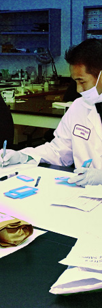 DNA technician, surrounded by multiple items of evidence to be processed in a laboratory.